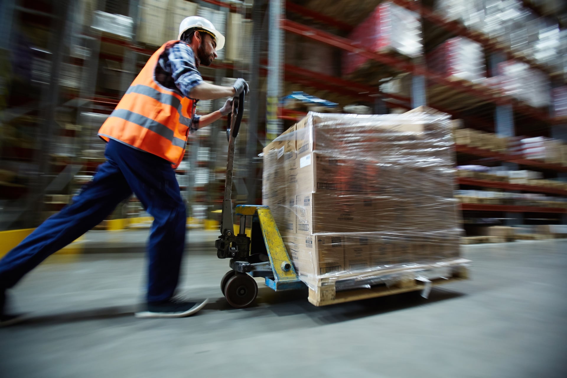 Male warehouse worker moving a pallet of packaged goods with a pallet jack.