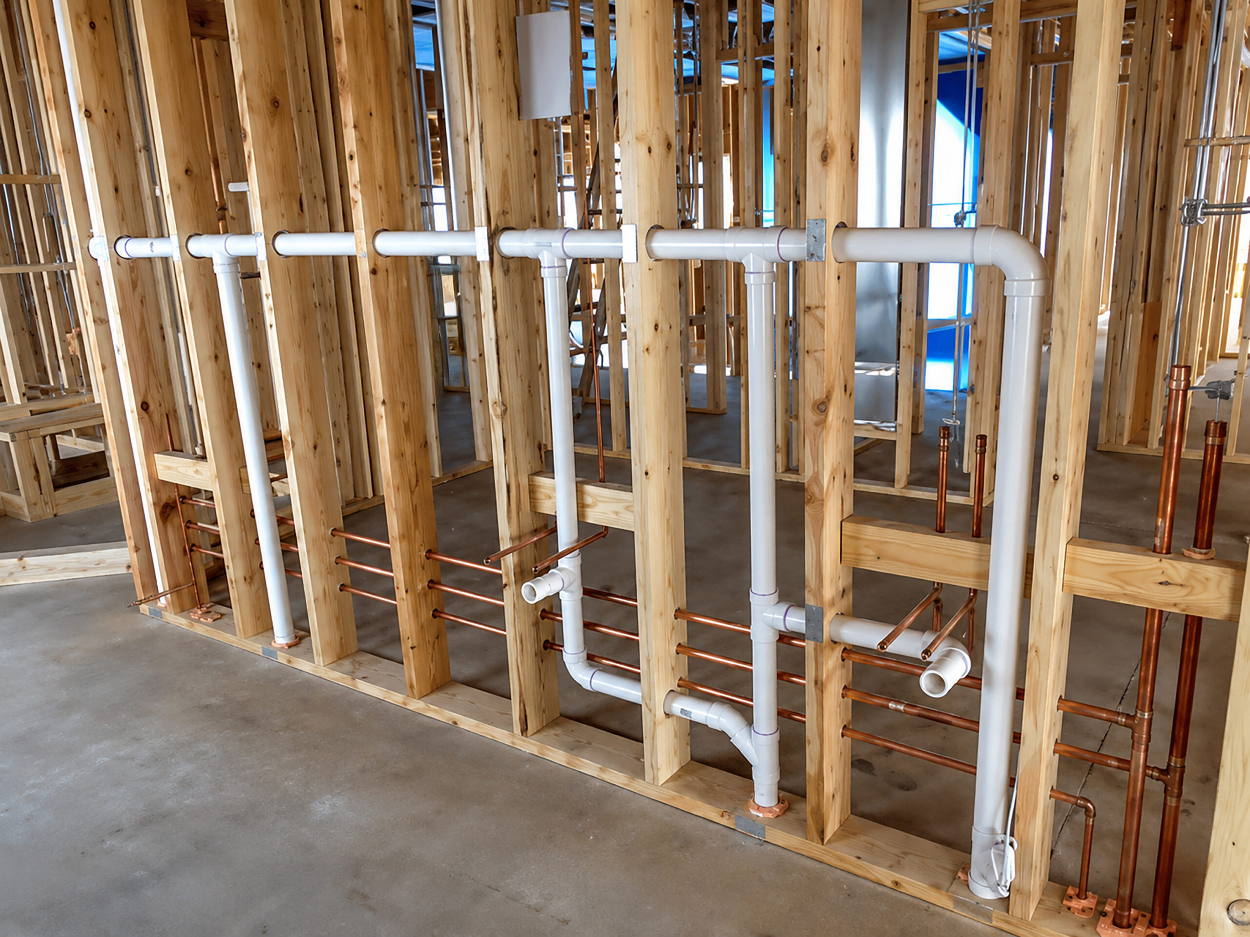 PVC and copper plumbing pipes installed within wood framing at a construction site.