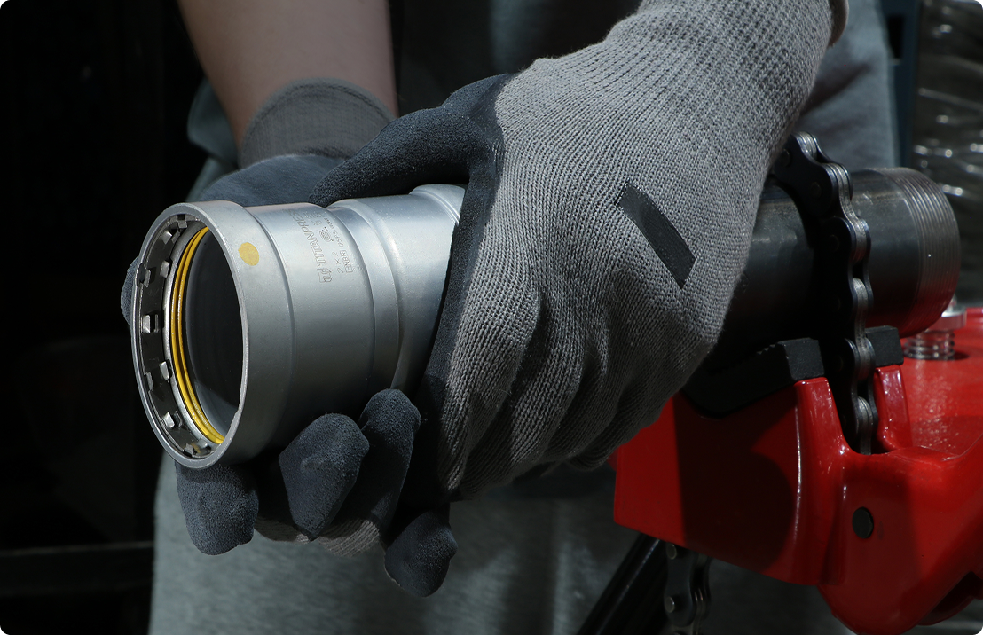 Worker installing a Titanpress carbon steel press fitting onto black pipe.