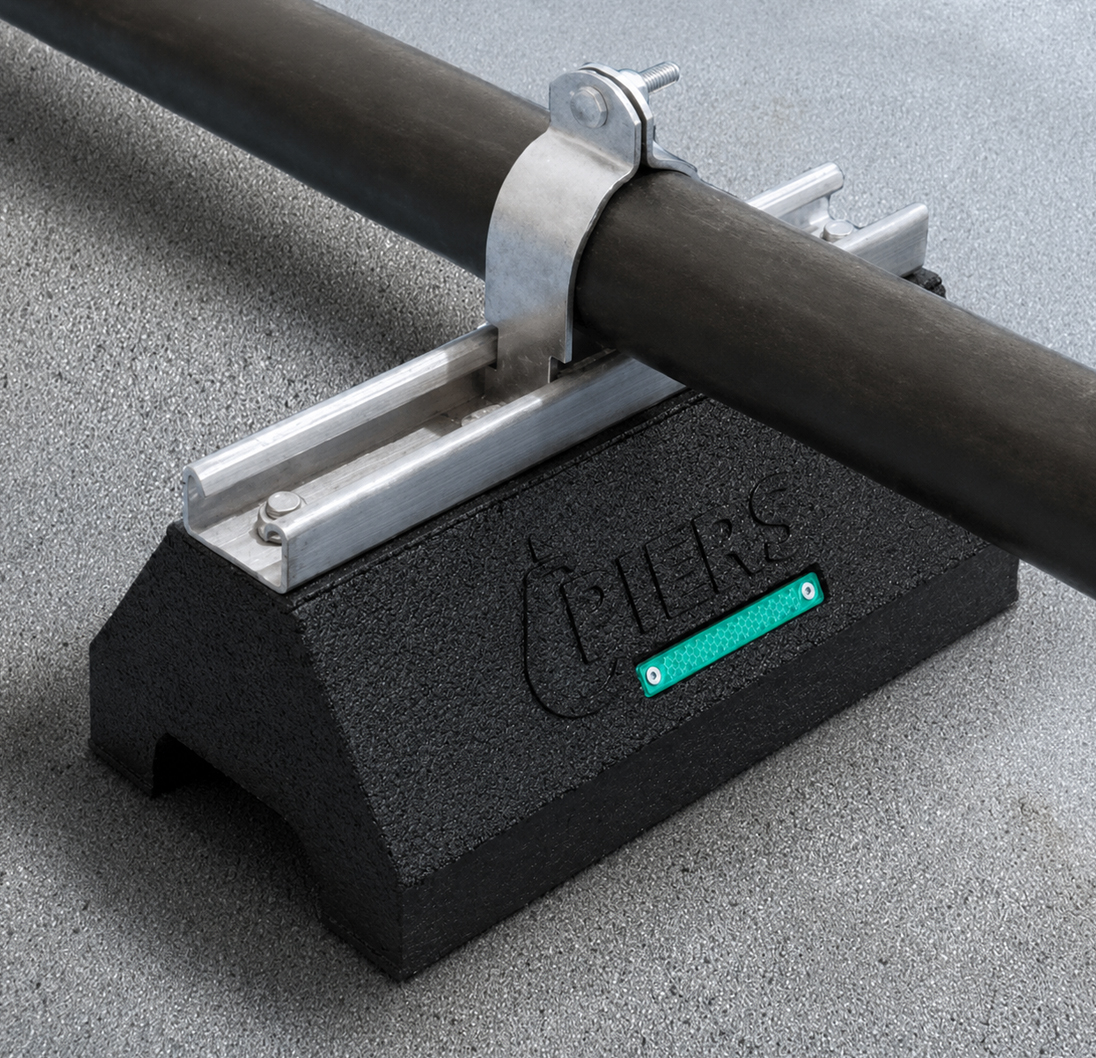 Piers rooftop pipe support block holding black piping and metal hardware.