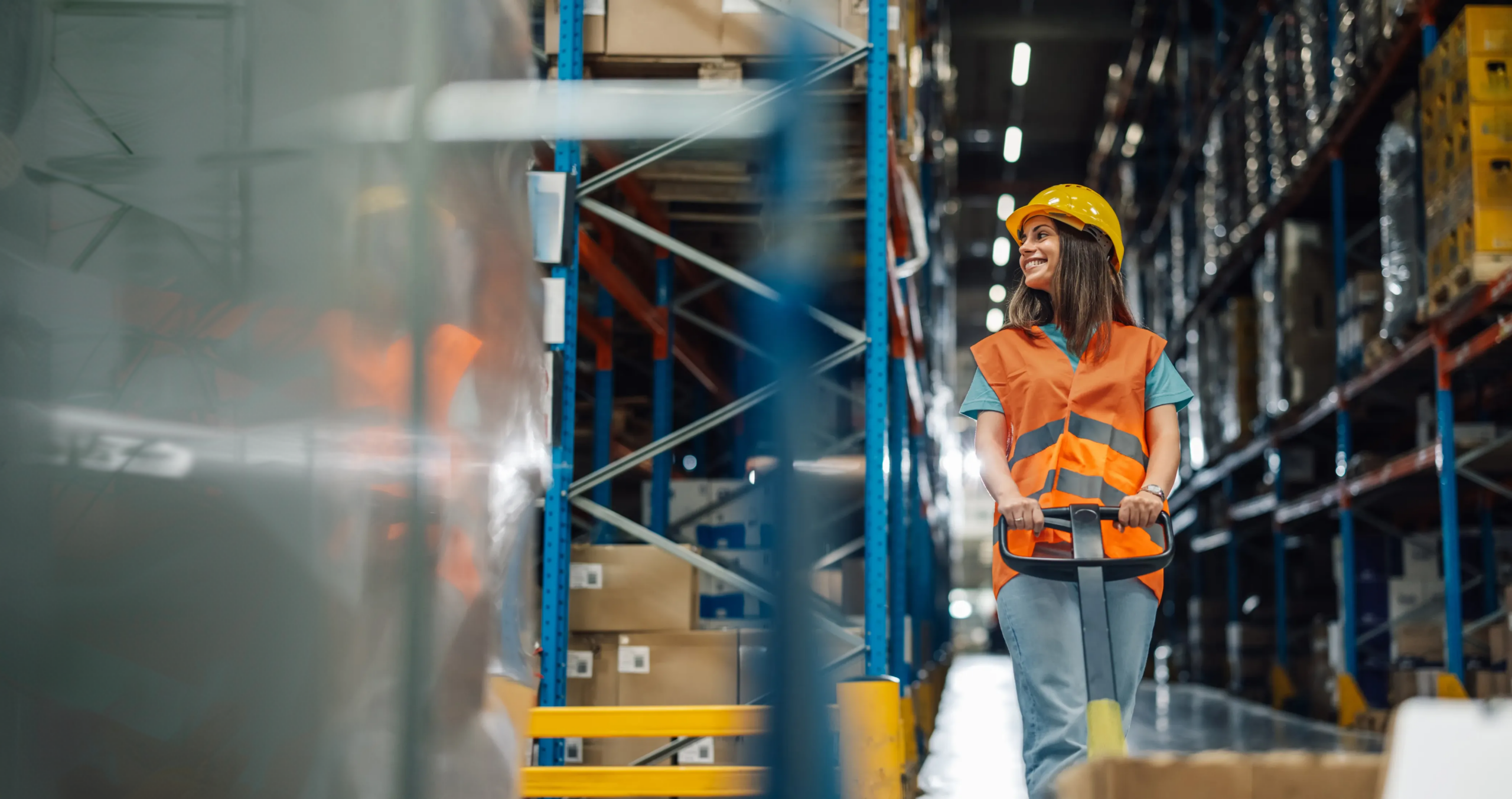 Female warehouse associate moves inventory through distribution center aisles with a pallet jack.