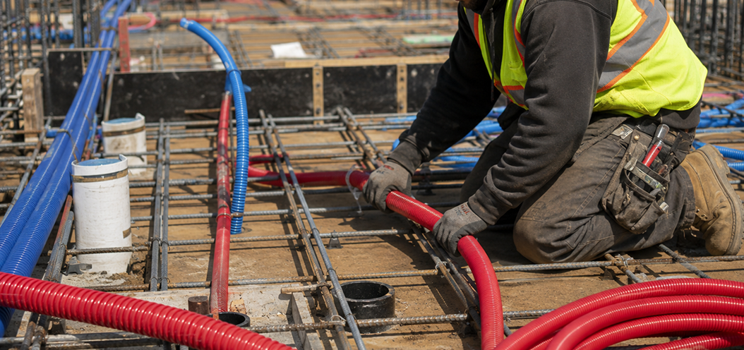 Worker installing red PEX tubing for a radiant heating system at a construction site.