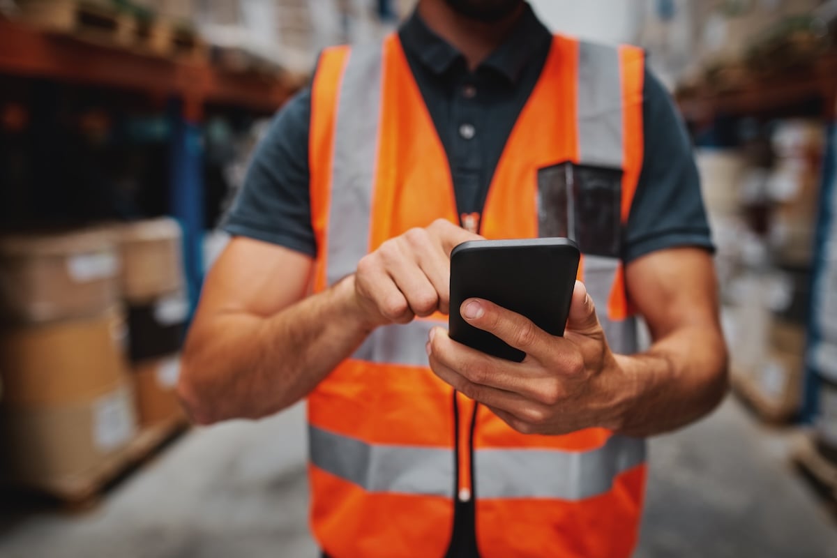 Warehouse worker using a smartphone to manage inventory and logistics operations.