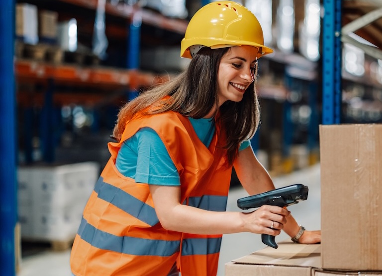 Warehouse worker scanning a cardboard box with a handheld barcode scanner.