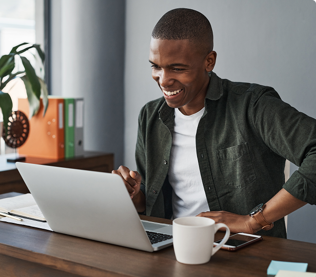 A man working on a computer at his desk in an office setting with a cup of coffee.