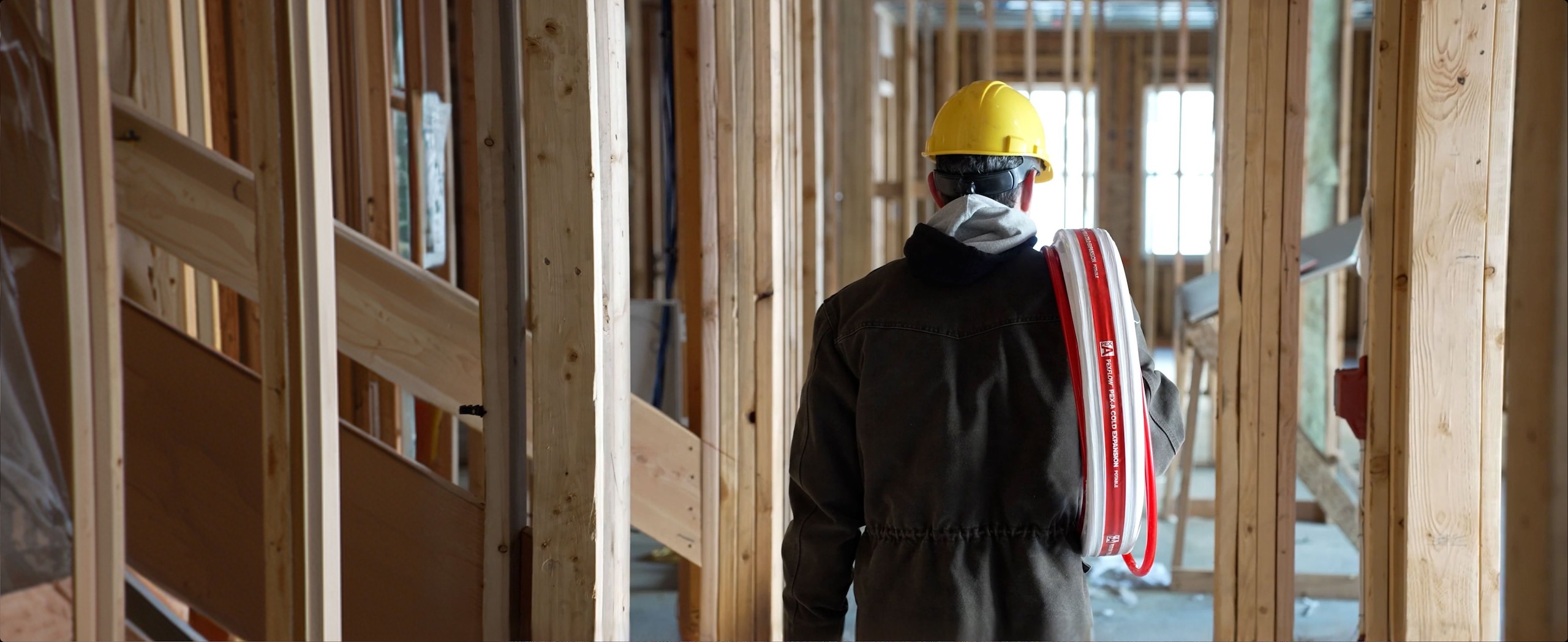 Construction worker carrying PEX tubing for a residential plumbing installation.